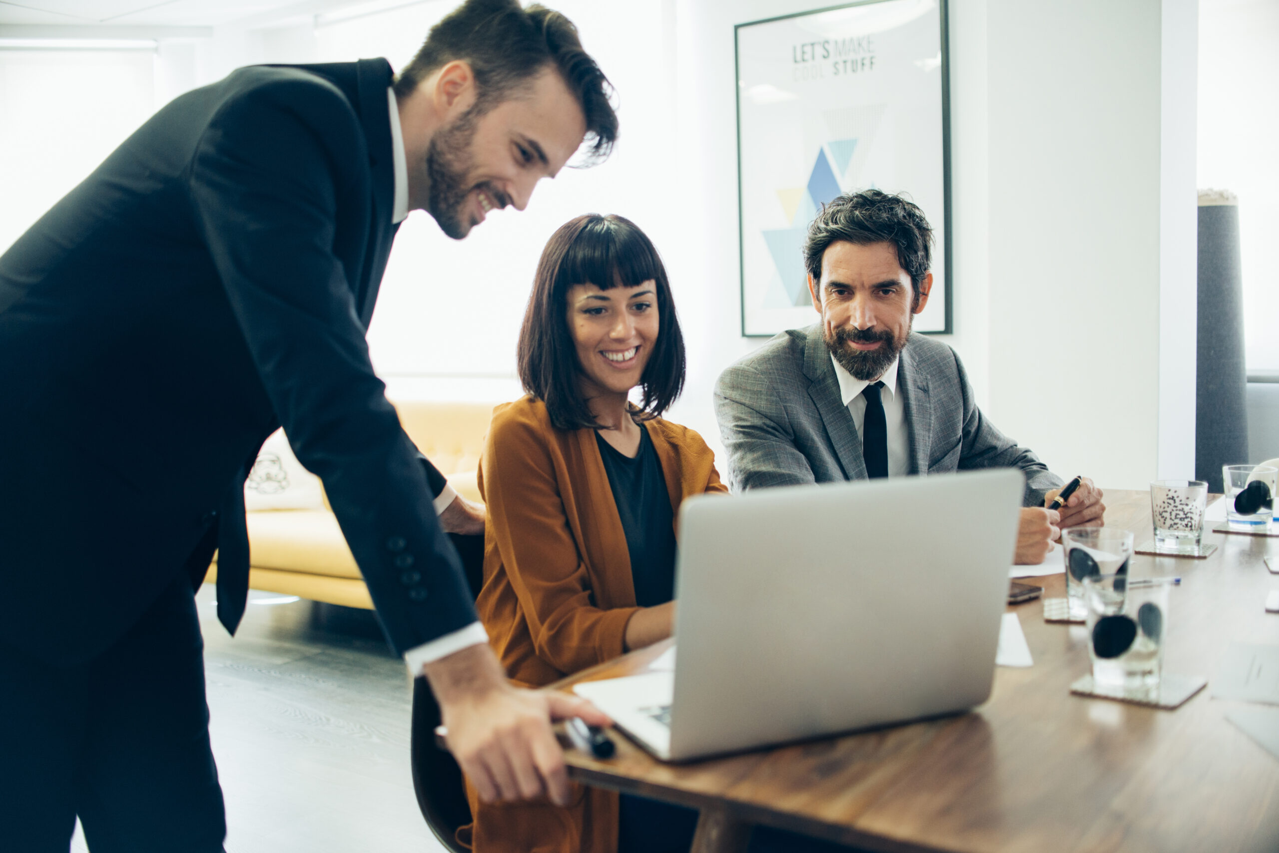 Three people two men and a woman working. a man and woman sitting on chair while one man standing three looking at laptop